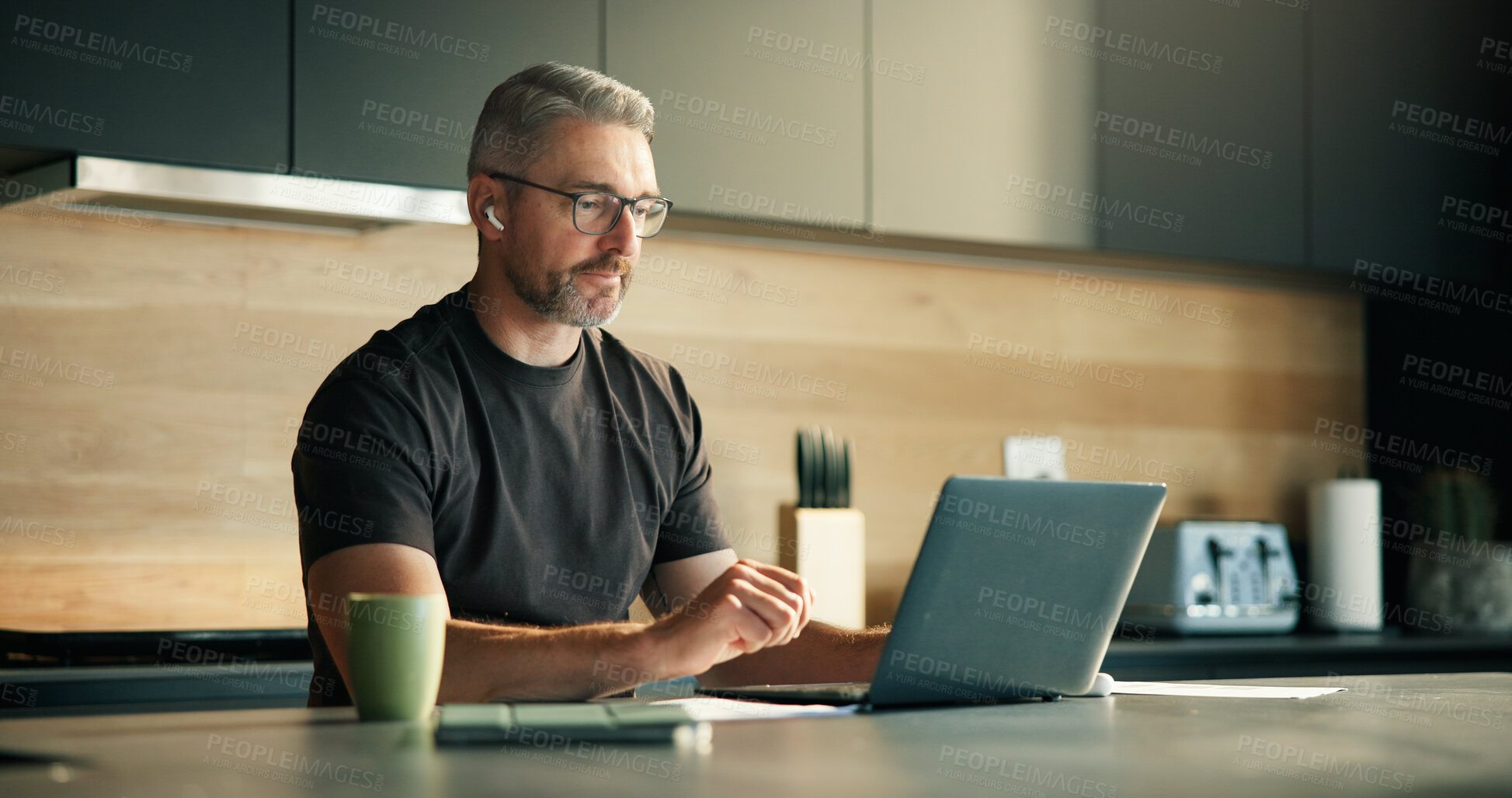 Buy stock photo Laptop, remote work and streaming with man in kitchen of home for planning, report or research. Computer, earphones and freelance with mature person in apartment for small business or startup review