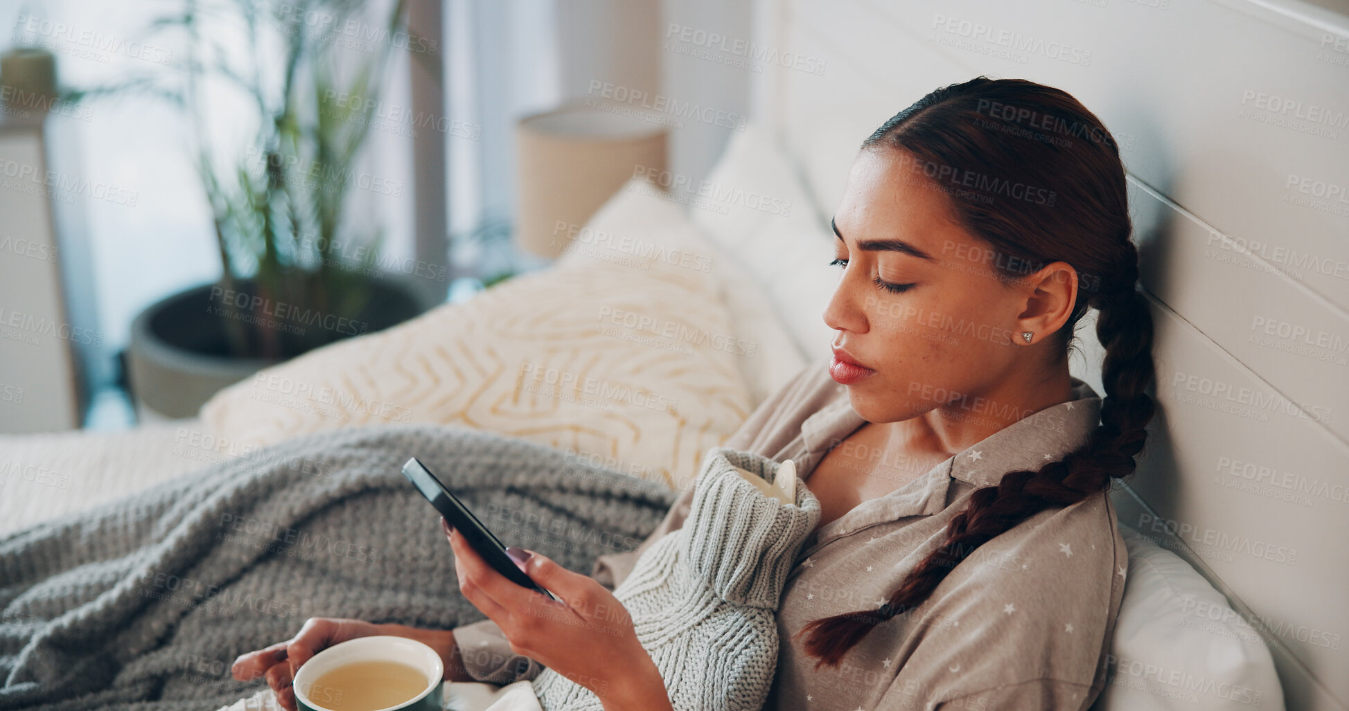 Buy stock photo Woman, phone and sick in bed with texting, herbal tea and hot water bottle for recovery in home. Person, smartphone and rest with drink for flu virus, mobile app or relax with chat on social media