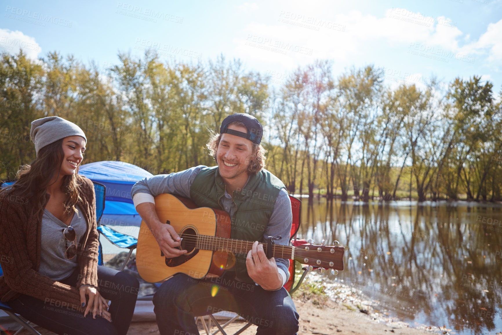 Buy stock photo Couple, camping outdoor and play guitar for love song, date and bonding together on vacation. String instrument, man and woman by tent in nature for romantic music, smile and relax on holiday by lake