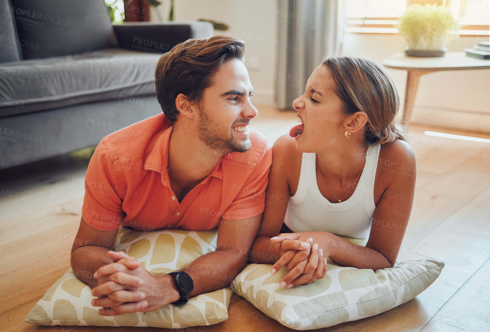 Buy stock photo Love, funny and happy couple relax on floor in home for care, bonding and playful with comic partner. Living room, man and woman with tongue out together for joke, comedy or silly face with cushions