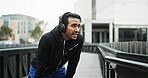 Headphones, athlete and break with running in city for workout rest, breathing or sweat with challenge. Runner, man and technology for training, fitness and exercise with podcast or streaming music