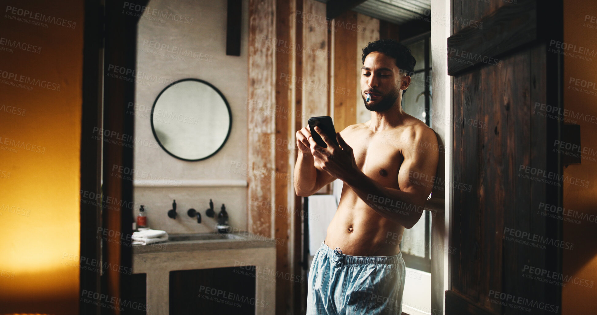 Buy stock photo Phone, brushing teeth and man in home for oral hygiene, wellness and morning news. Mobile, cleaning mouth and shirtless person by bathroom doorway with dental app, health and reading message online