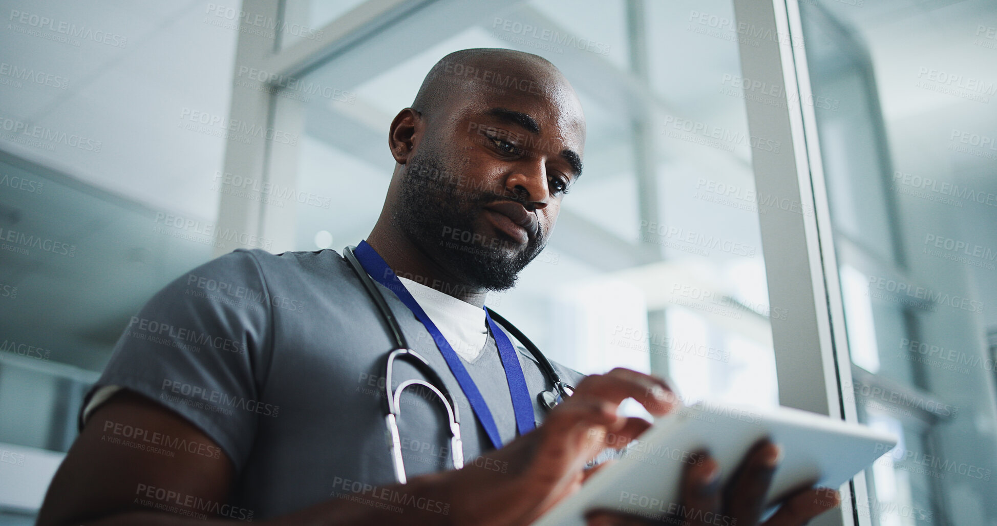 Buy stock photo Black man, doctor and reading with tablet in hospital for research, medical report and test results. Below, male person and digital for healthcare history, treatment planning and surgery schedule