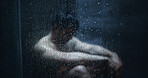 Man, dark shower and sad by glass in home, stress and mental health with ptsd for bad memory. Person with depression, blur and anxiety with water drops, window and frustrated in bathroom at house