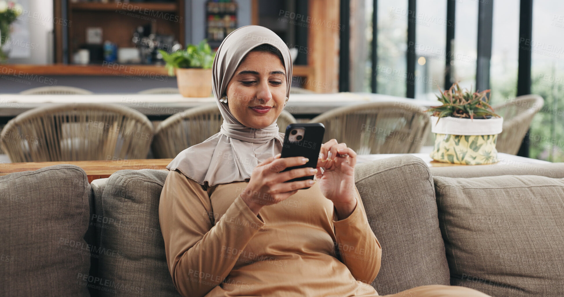 Buy stock photo Muslim woman, phone and happy with texting on sofa in home, scroll or check notification in lounge. Islamic person, smartphone and smile with hijab for contact, web chat and and social media in house