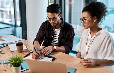 Buy stock photo Cropped shot of two young businesspeople sitting together and having a meeting over polaroids in the office