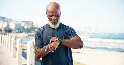 Buy stock photo Black man, exercise and smart watch by beach with fitness app, heart rate tracker and step count. Mature person, workout break and timer by ocean with tech, monitor training or wellness on promenade.