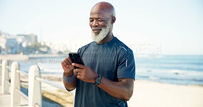 Buy stock photo Old man, scroll and fitness by beach with phone, social media and notification for wellness app. Senior black person, typing and tech on promenade outdoor with text message, exercise or workout rest.