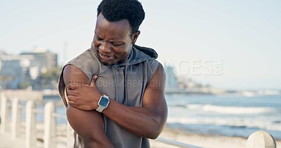 Buy stock photo Black man, shoulder pain and fitness with injury on beach promenade on break with sore muscle in summer. Person, runner and fatigue with joint strain, exercise or rest with space on seaside boardwalk