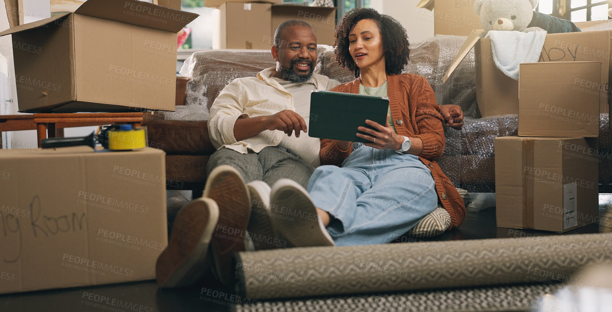 Buy stock photo Boxes, relax and tablet with couple in new home together for planning or property investment. App, conversation and real estate with African people on apartment floor for moving house or relocation