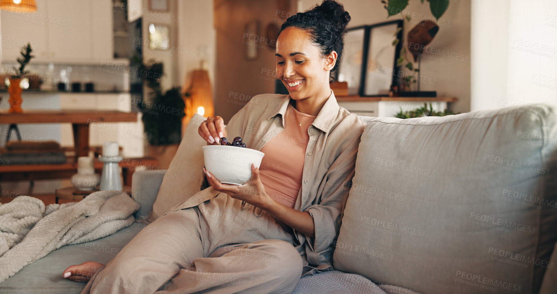 Buy stock photo Grapes, relax and smile of woman on sofa in living room of home for break, chilling or me time. Bowl, eating and fruit with happy person in apartment for morning meal, snack or weekend nutrition