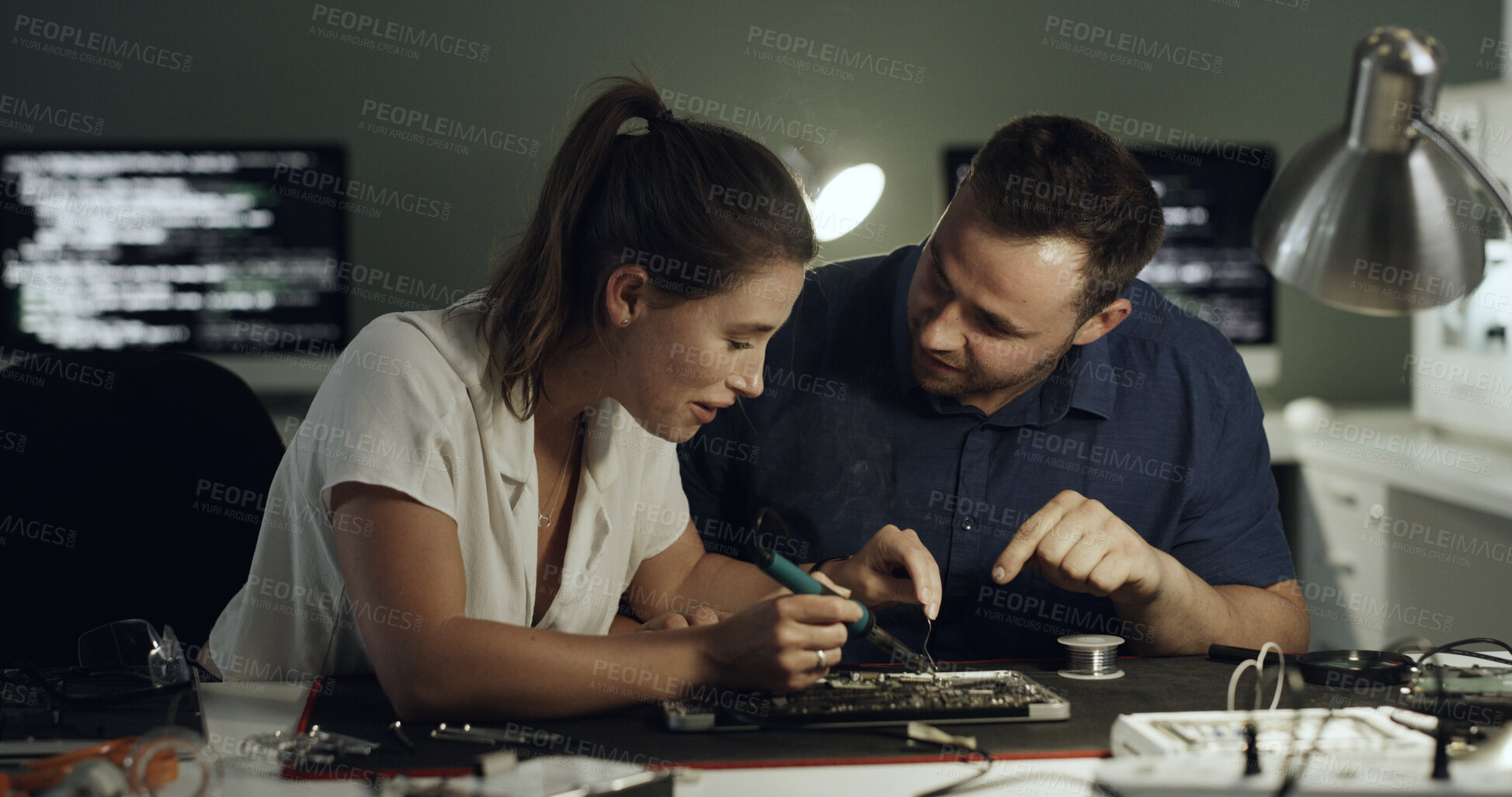 Buy stock photo Soldering, night or team in workshop with circuit board, repair or wiring guidance in hardware check. Electronics, people or engineers with tech, maintenance collaboration or system fix in evening.