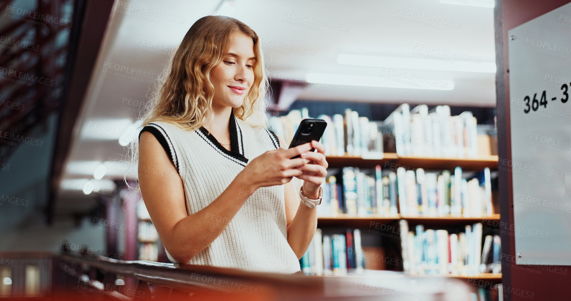 Buy stock photo Woman, student and texting with phone at library for education, smile and contact on web at college. Girl, smartphone and happy with chat, mobile app or social media on study break at university