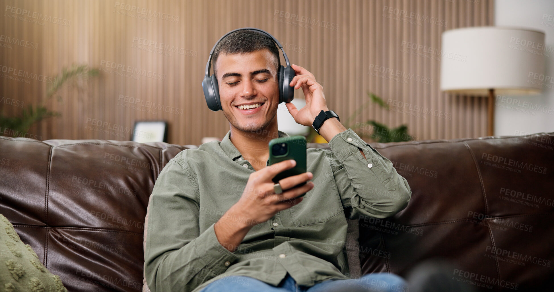 Buy stock photo Man, phone and happy with headphones on sofa for streaming, relax and sound in living room at house. Person, smartphone and listen to music with subscription, mobile app or texting on couch in home