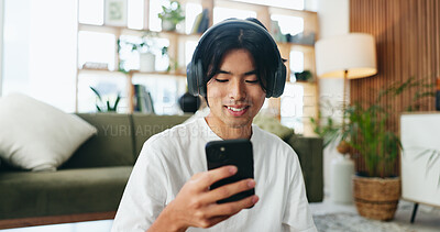 Buy stock photo Headphones, reading and Asian man with phone in living room, streaming podcast and social media video. Smile, home and person with tech for subscription, watch movie trailer and listen to audiobook