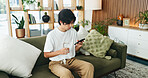 Phone, relax and water with Asian man on sofa in home living room for hydration or social media. Break, drink and glass with person scrolling mobile app for browsing, connection or online search
