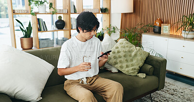 Buy stock photo Phone, relax and water with Asian man on sofa in home living room for hydration or social media. Break, drink and glass with person scrolling mobile app for browsing, connection or online search
