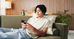 Reading, text and Asian man on sofa with phone, internet search and communication on online platform. Scroll, digital and person in house with tech, social media update and message on virtual app.