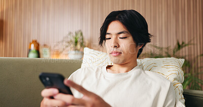 Buy stock photo Reading, text and Asian man on couch with phone, internet search and communication on online platform. Scroll, digital and person in house with tech, social media update and message on virtual app.