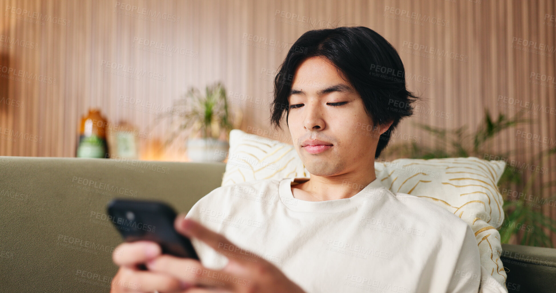 Buy stock photo Reading, text and Asian man on couch with phone, internet search and communication on online platform. Scroll, digital and person in house with tech, social media update and message on virtual app.
