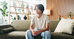 Thinking, sad and man on sofa in home with regret for decision or choice with mental health. Anxiety, uncertain and Asian male person with reflection for mistake, failure or bad news in living room.