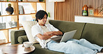 Education, laptop and smile of Asian man on sofa in home living room for distance learning. Computer, online study and streaming with happy university student in apartment for development or growth