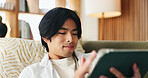 Education, reading and tablet with Asian man on sofa in home living room for distance learning. App, online study and scrolling with university student in apartment for development or growth