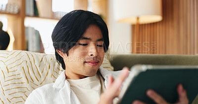 Buy stock photo Education, reading and tablet with Asian man on sofa in home living room for distance learning. App, online study and scrolling with university student in apartment for development or growth