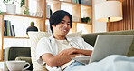 Laptop, smile and study with Asian man on sofa in home living room for distance learning. Computer, online education and streaming with happy university student in apartment for development or growth