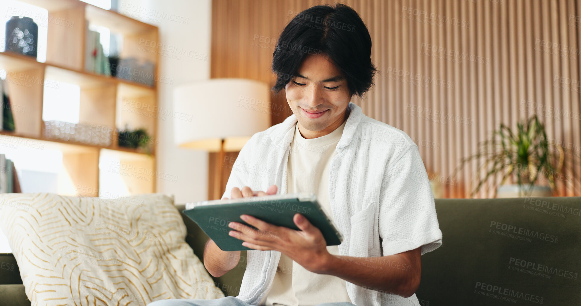 Buy stock photo Smile, study and tablet with Asian man on sofa in home living room for distance learning. App, online education and streaming with happy university student in apartment for development or growth