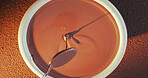 Spoon, dripping and bowl with chocolate for production, smooth texture and tempered mixture for baking. Above, gourmet process and cocoa with utensil for dessert preparation, refined liquid or mixing