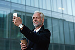 Senior businessman using smartphone taking photo ins city holding coffee