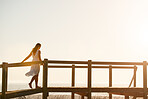 Beautiful woman wearing white dress walking on wooden beach walkway