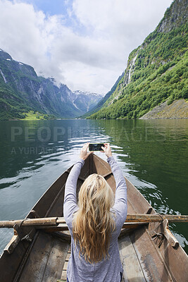 Buy stock photo Mountain, woman and river with boat for photography, travel and nature for holiday or vacation. Person, journey and rowing on lake for sightseeing, back or picture on phone for trip in Norway 