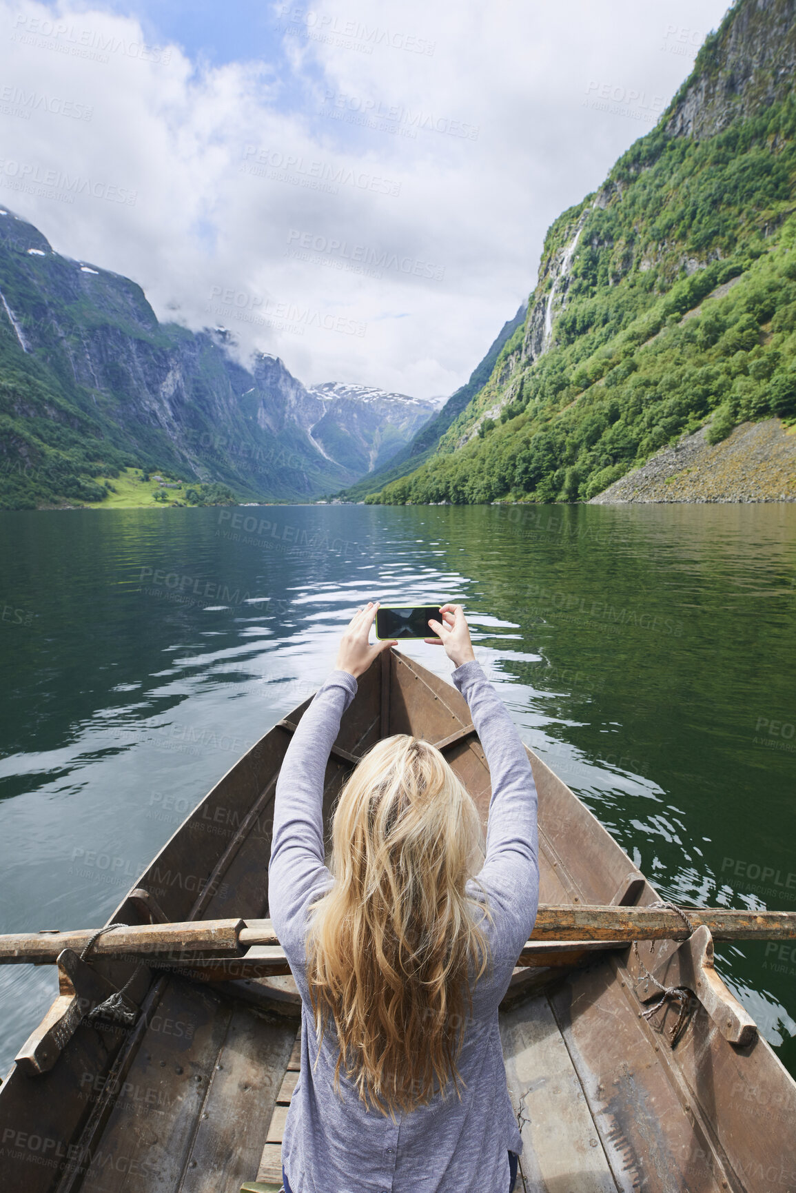Buy stock photo Mountain, woman and river with boat for photography, travel and nature for holiday or vacation. Person, journey and rowing on lake for sightseeing, back or picture on phone for trip in Norway 