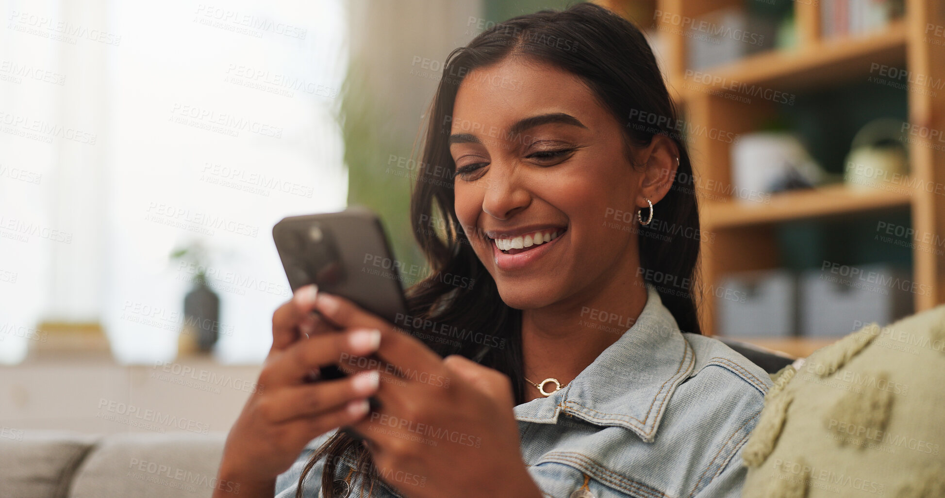Buy stock photo Woman, laugh and scroll on couch with phone, funny online dating profile and text message notification. Happy, Indian person and relax in house with tech, humor and mobile app for social media joke.