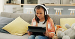 Girl, child and tablet on couch with headphones, browsing website and streaming service for cartoon. Kid, relax and watch movie in house with audio tech, digital app or film series for entertainment.