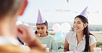 Happy people, family and birthday with party hat for outdoor celebration together at table. Excited, group or laughing with smile, balloons or milestone for another year, wishes or social gathering