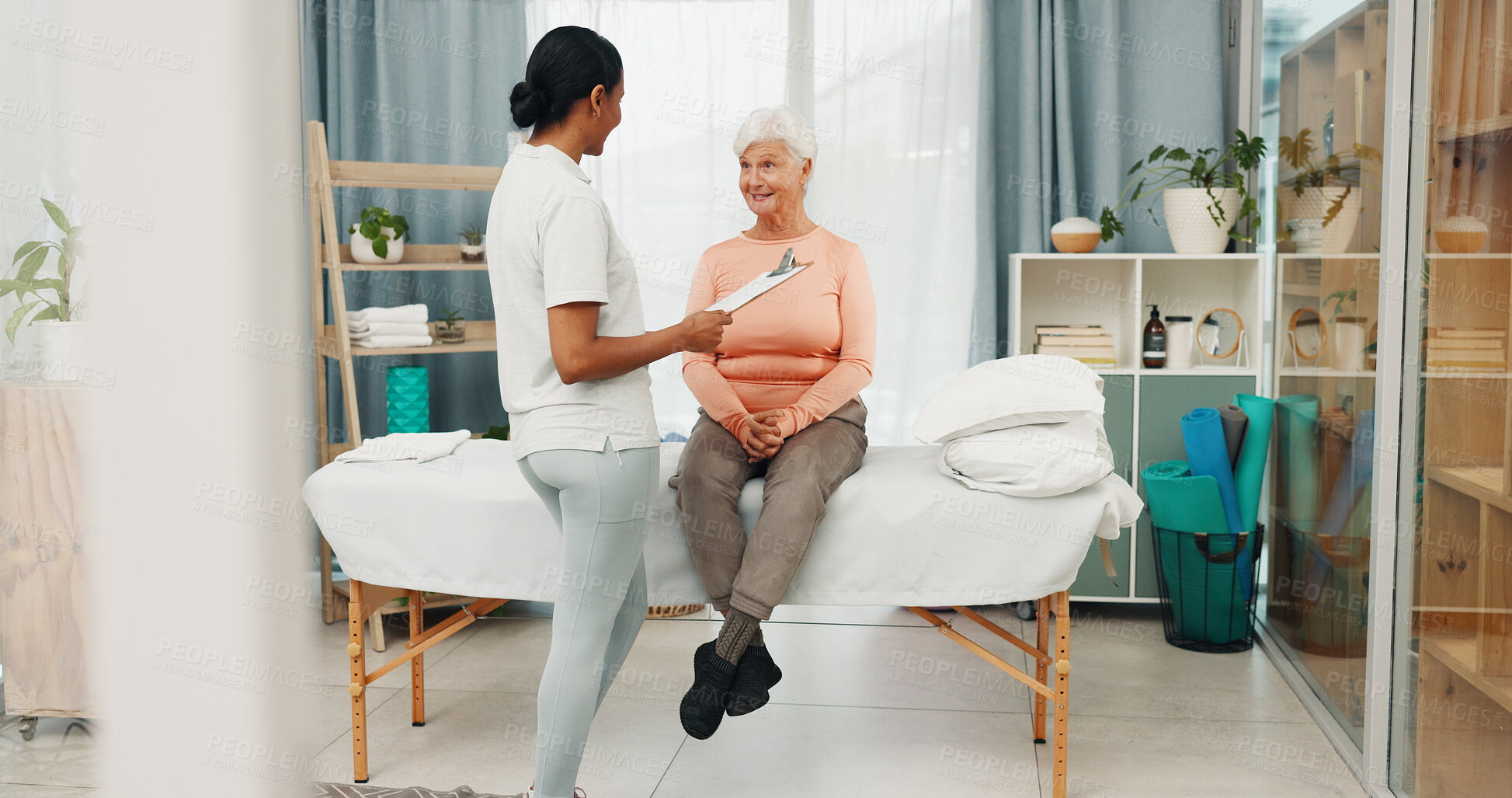 Buy stock photo Old woman, physiotherapy and discussion with clipboard, smile and good news for healing at clinic. People, patient and healthcare professional with report, feedback and happy on bed for consultation