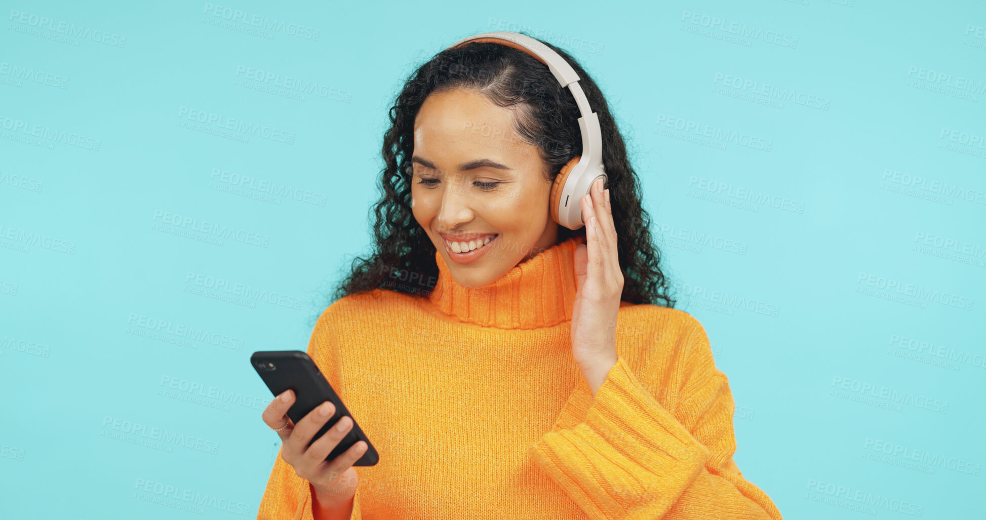 Buy stock photo Smile, phone and woman with headphones in studio for online streaming, music app and subscription. Space, happy and person on smartphone listening to audio, radio and playlist on blue background