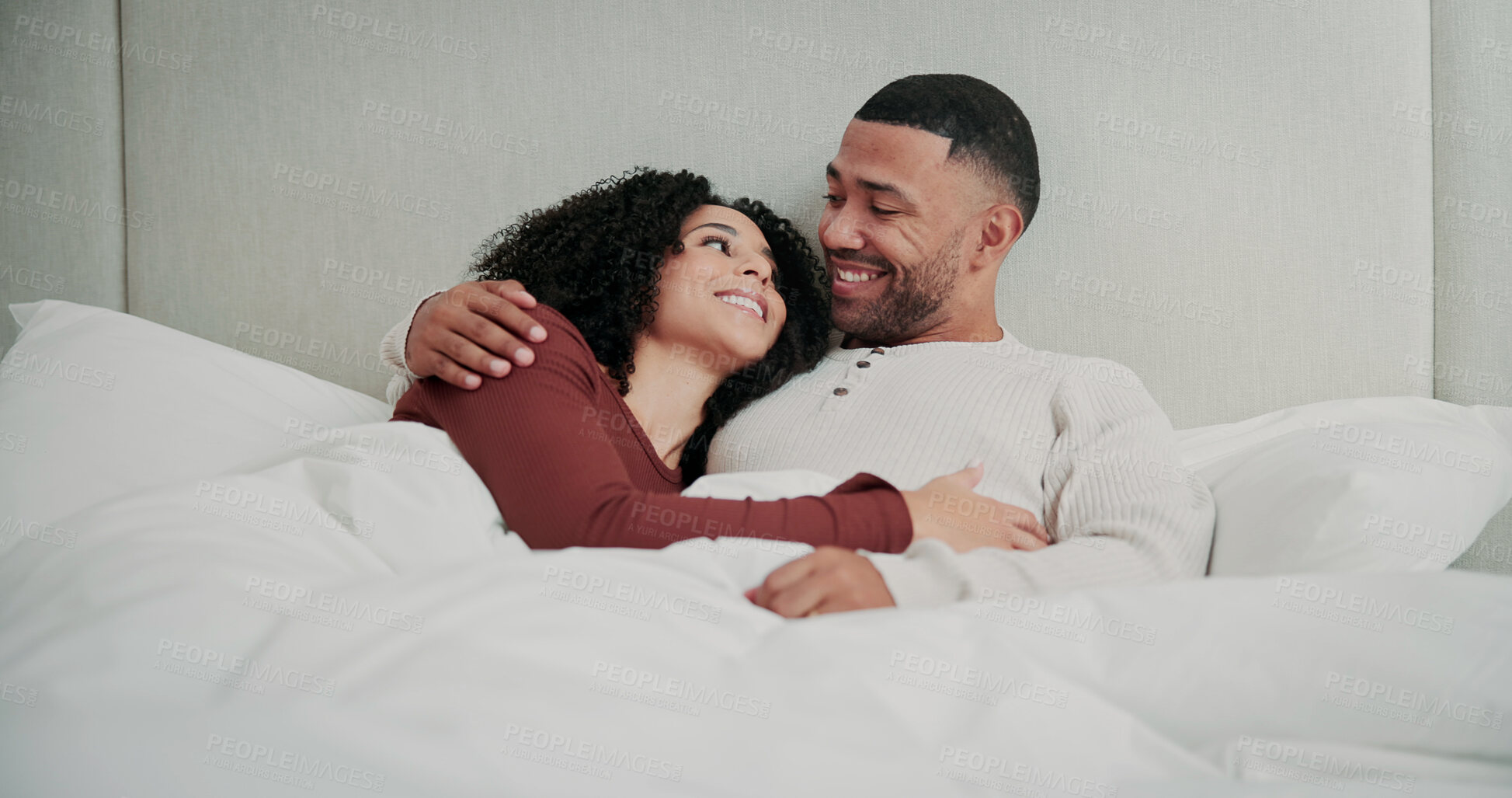Buy stock photo Love, cuddle and couple with smile in bed on weekend, romantic morning and conversation for bonding. Relax, support and happy people with hug for emotional connection, care and chat in home together