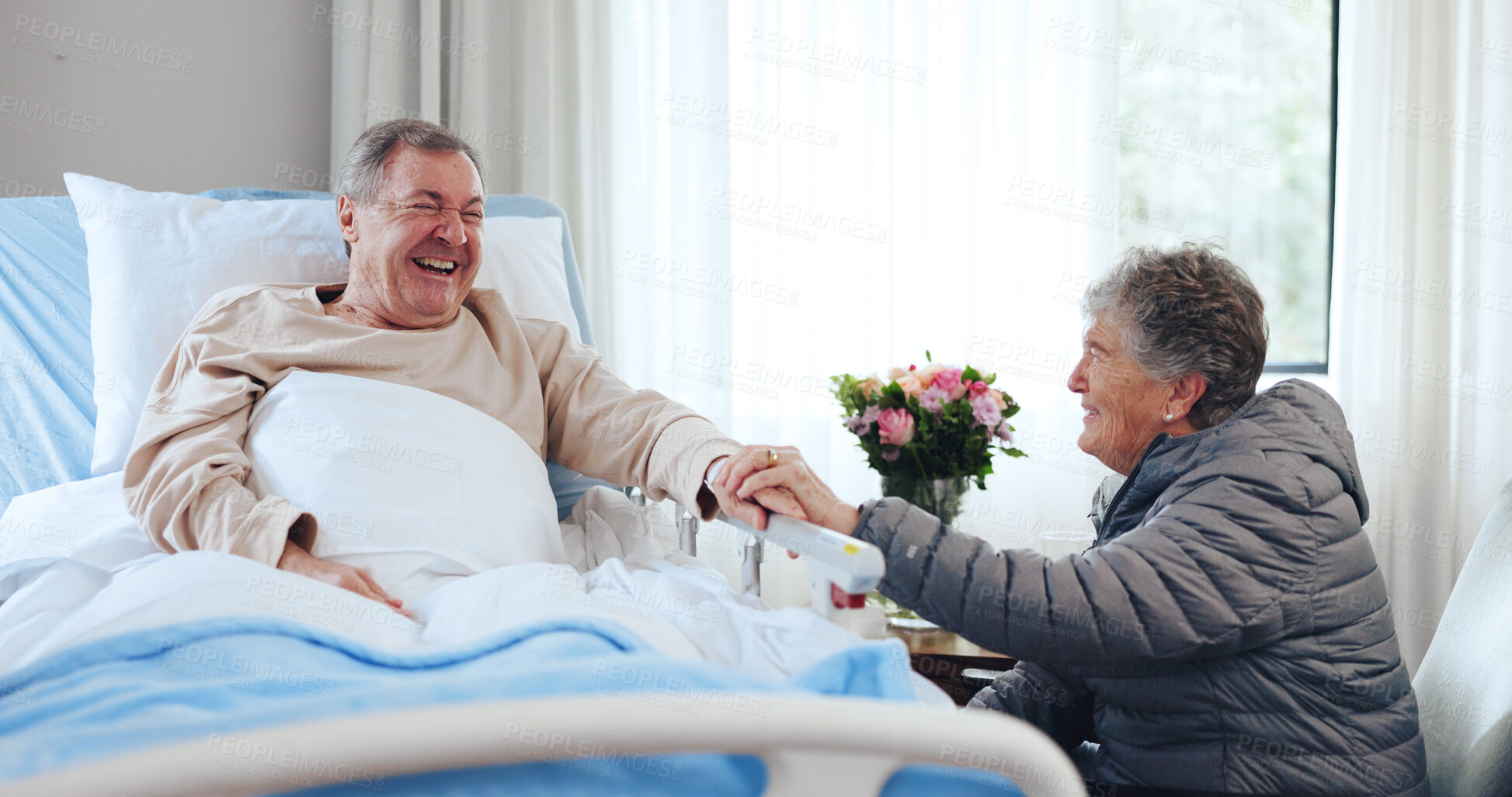 Buy stock photo Laugh, old couple and holding hands in hospital for support, funny conversation and visit for comfort. Smile, care and senior people with humor in medical clinic, talking and flowers for recovery