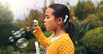 Outdoor, child and blowing bubbles in nature, growth and development with activity on weekend break. Park, entertainment and girl with toy for soap balloons, fine motor skills or playing game for fun