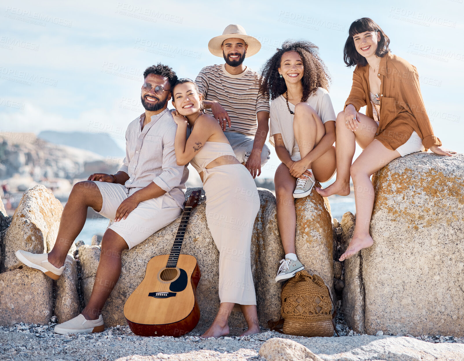 Buy stock photo Happy people, portrait or friends on beach for outdoor bonding, social gathering or vacation. Group, community or smile with guitar for weekend trip, summer holiday or travel on ocean rocks by shore