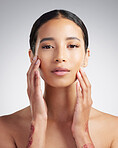 Portrait of a beautiful mixed race woman touching smooth soft skin in a studio. Hispanic model with healthy natural glowing skin looking confident against grey copyspace while doing routine skincare