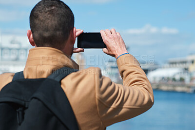 Buy stock photo Photo, back and man in town with phone, online memories or post update on weekend travel. Digital, tourism and male person at harbor with tech, social media picture or memory capture on outdoor trip.