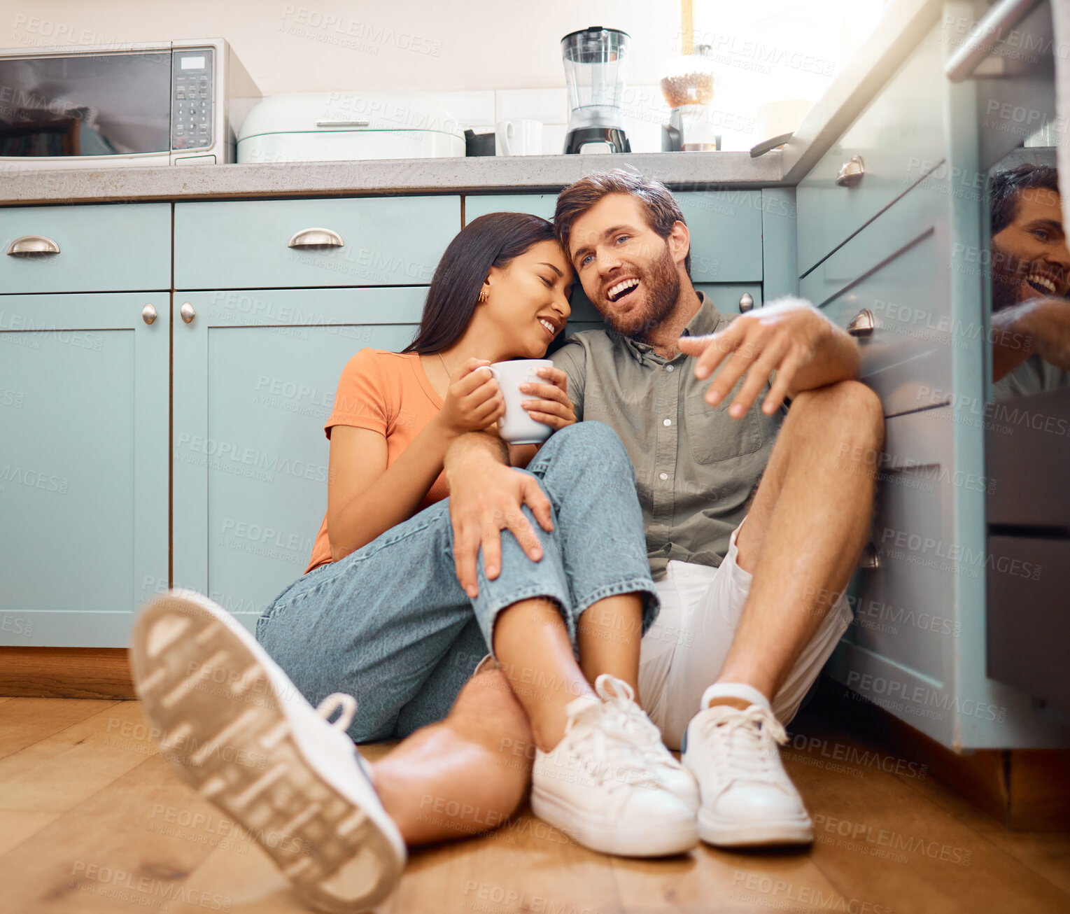 Buy stock photo Couple, happy and relax with drink in kitchen with conversation, bonding and interracial relationship. Cuddle, talking and man with woman on floor for break, commitment and trust with coffee in home