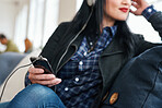 Woman using smartphone listening to music on mobile phone wearing headphones sitting on sofa at home
