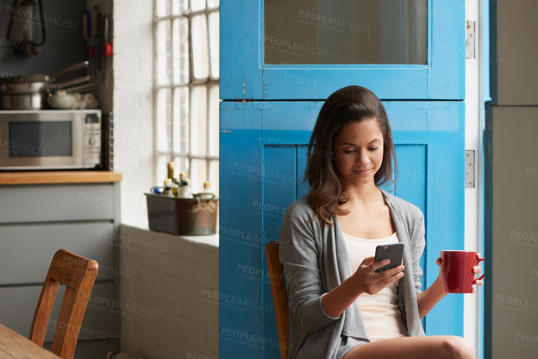 Buy stock photo Woman, phone and texting with coffee cup in kitchen, scroll or web chat for online dating in home. Person, relax and typing with mobile app, smile and drink on social media with beverage in house