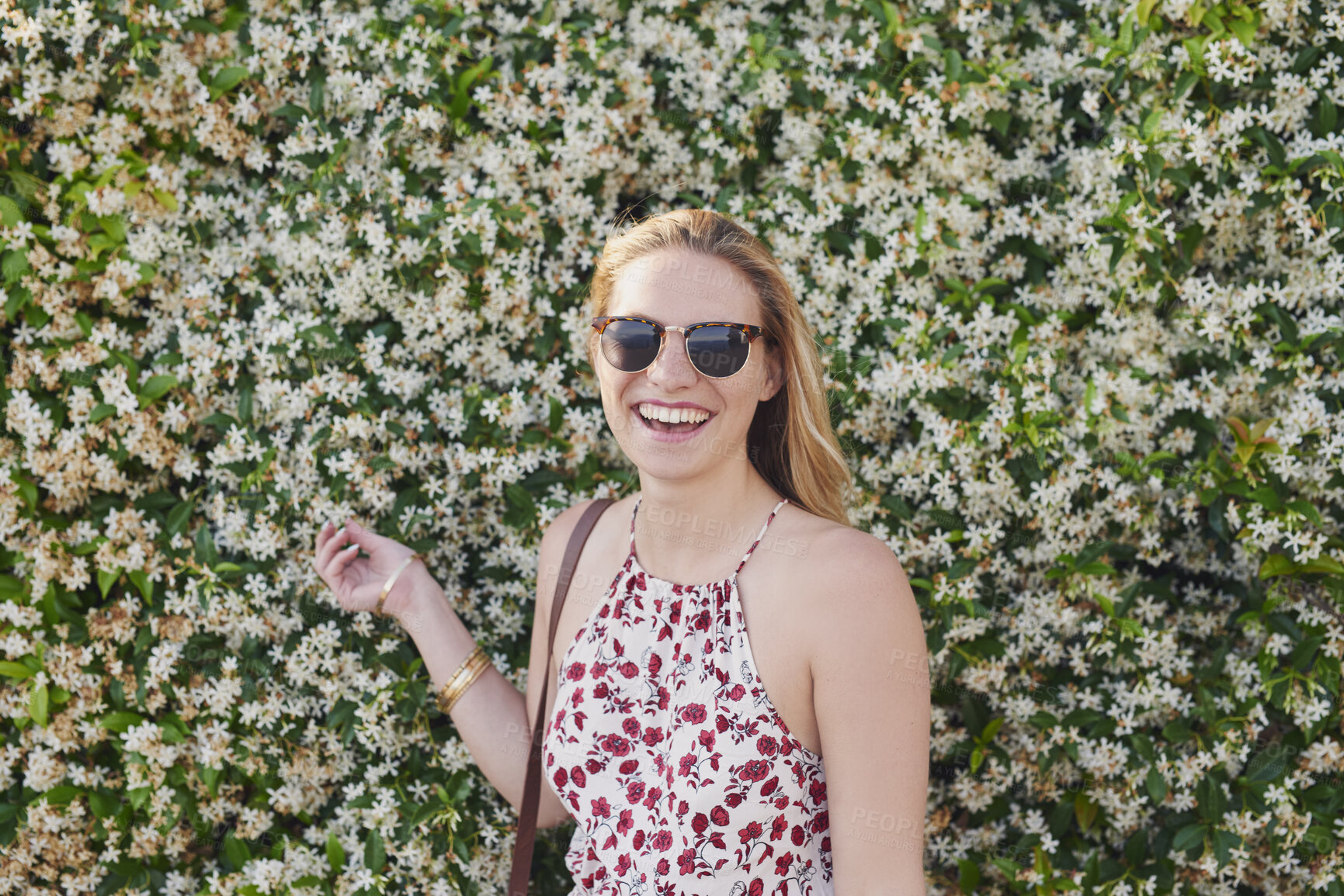 Buy stock photo Outdoor, laughing or woman with sunglasses for travel, eco tourism or sightseeing for spring vacation. Botanical park, holiday or happy person with shades by flower wall, space or nature growth